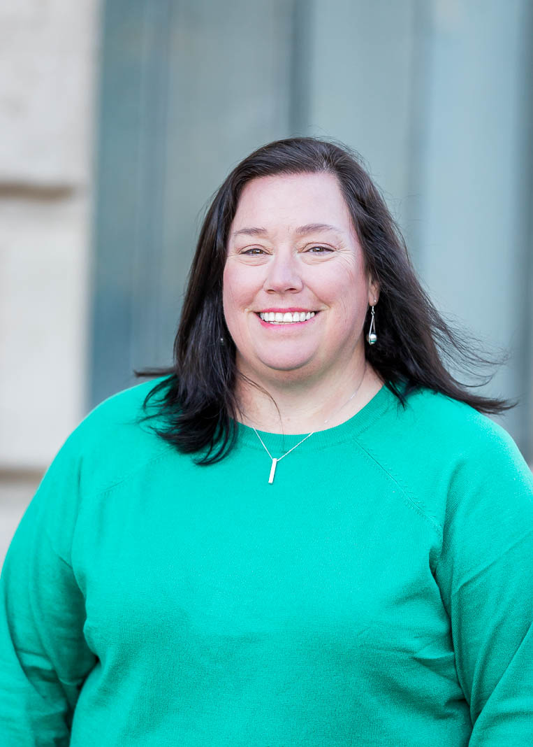 Lisa, a middle aged white woman, with shoulder length dark brown hair, wears a teal top, and smiles in a headshot.