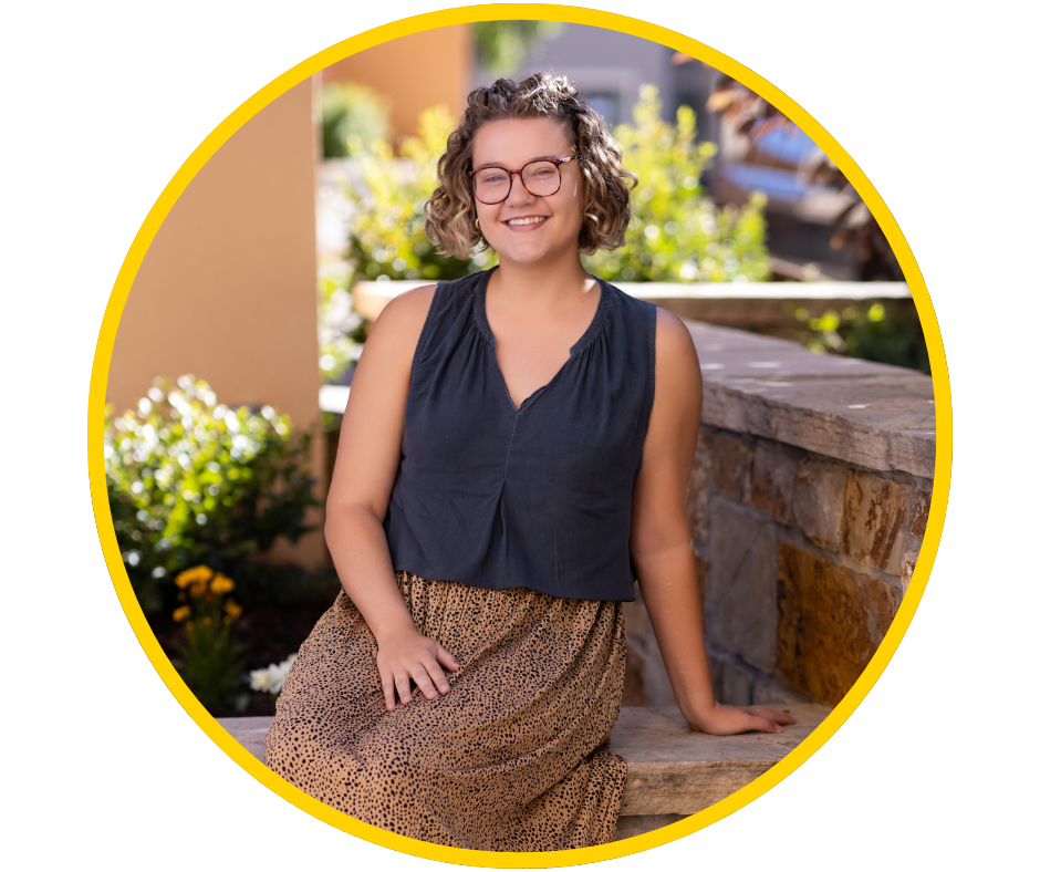 Dani, a young woman with light skin, short blonde hair, and glasses, smiles wearing a black tanktop and cheetah skirt.