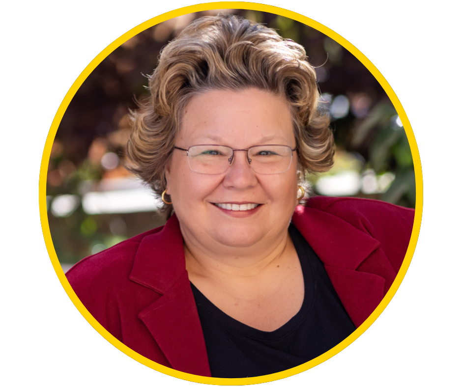 Cheryl, a middle aged woman with light skin smiles with short blonde hair and a red blazer.