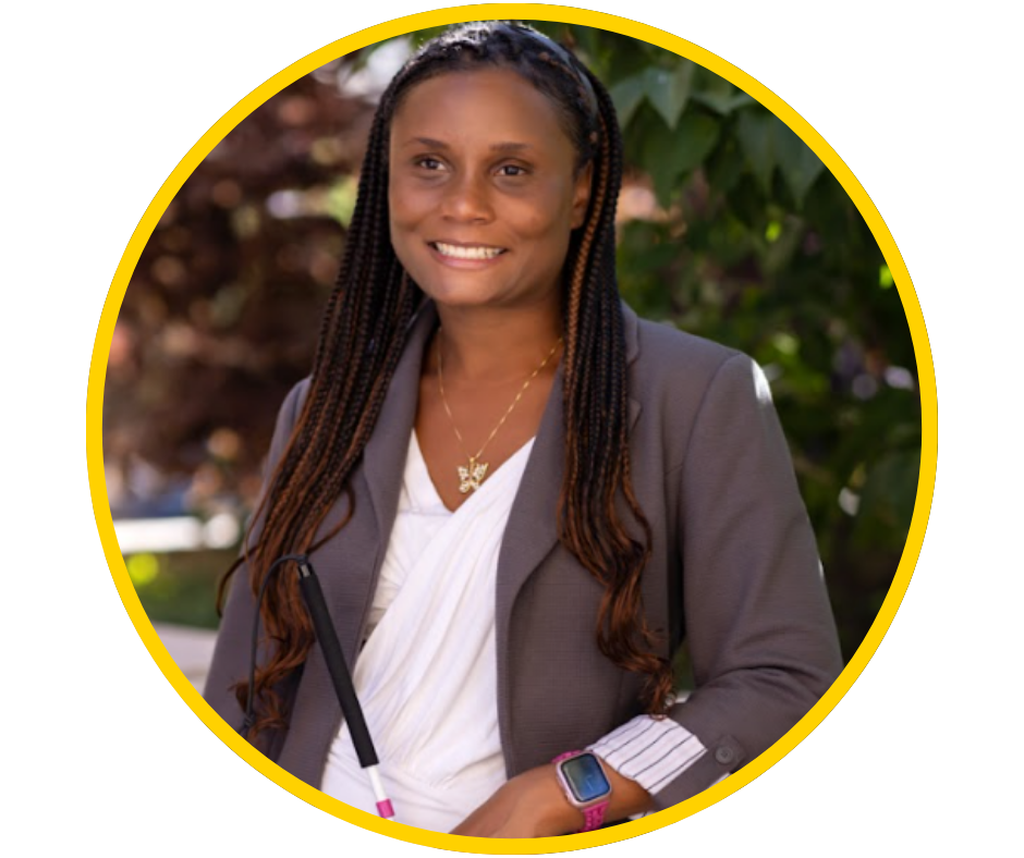 Serina, a young woman with dark skin and long braids smiles holding her white cane, in a grey blazer.