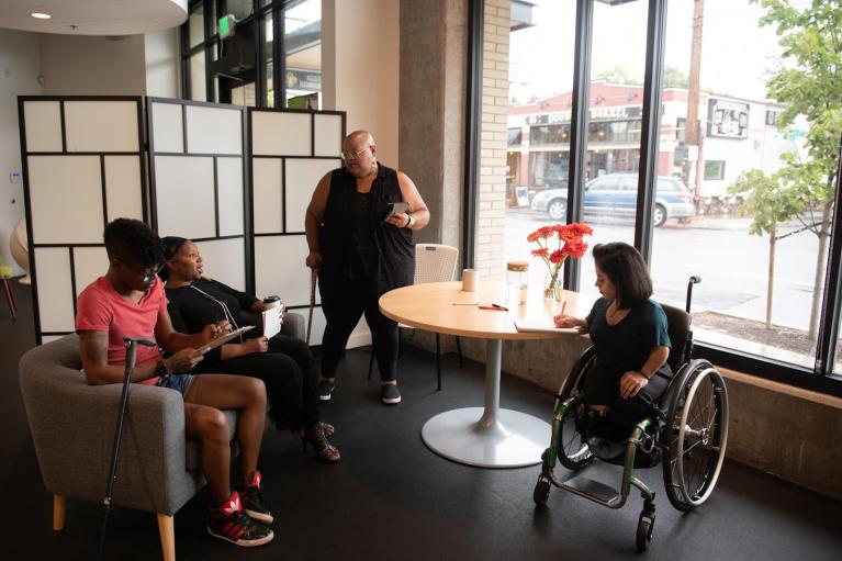 a group of people of color, one using a cane and one in a wheelchair, in an office setting