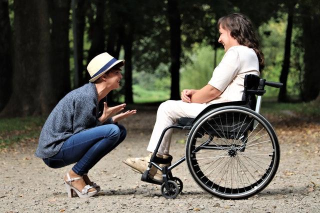 two women talking outside, one in a wheelchair and another crouching down to talk