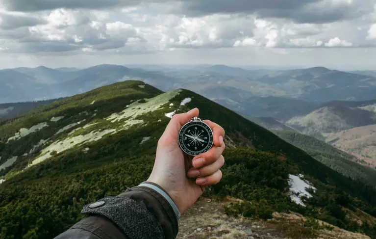 hand holding a compass with a view of mountains
